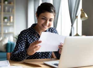 A woman smiling while reading a letter at her desk