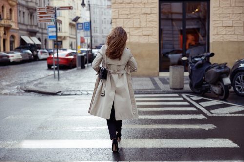 Back view of a woman wearing a trench coat crossing a city street