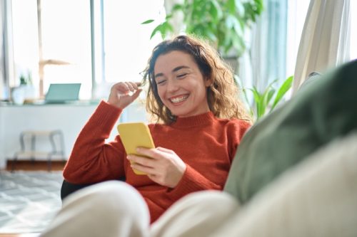 woman laughing while looking at her phone on the couch