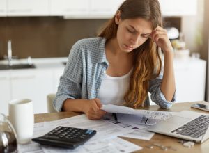 woman looking at bills with her computer and a calculator in front of her