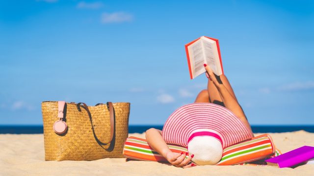 Woman in sun hat reading on a beach