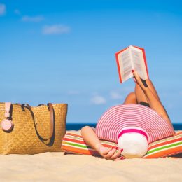 Woman in sun hat reading on a beach