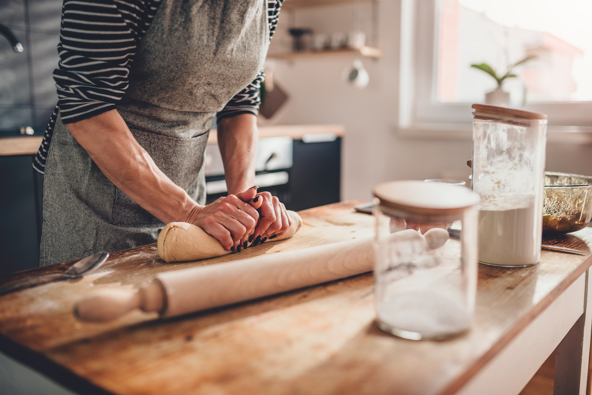 Woman standing in kitchen at a wooden countertop kneading dough