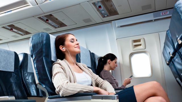 A woman lying back in a plane seat with her eyes closed and headphones in