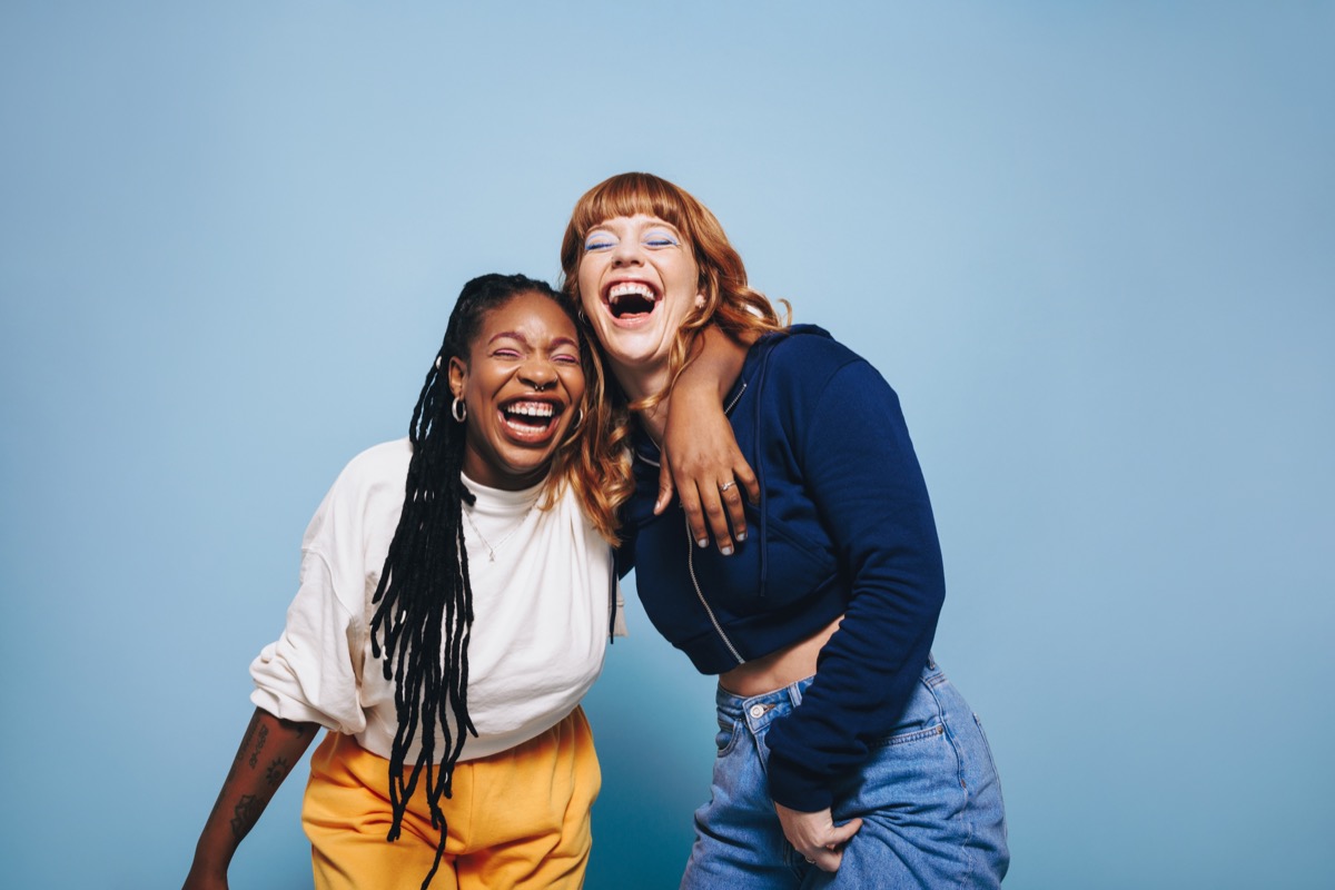 two young women laughing with arms around each other on a blue background