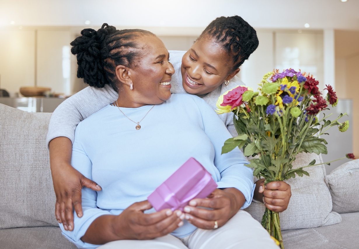 A woman receiving a gift, flowers, and a hug from her younger daughter