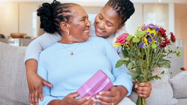 A woman receiving a gift, flowers, and a hug from her younger daughter