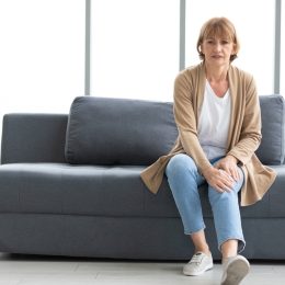 senior woman suffering from knee ache on sofa