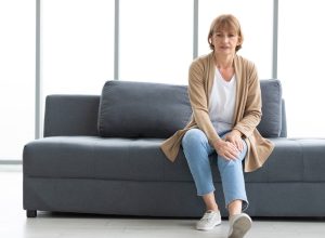senior woman suffering from knee ache on sofa