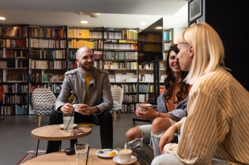 two young women and a young man chatting and drinking coffee in a library