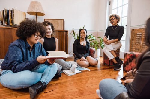 Group of young women reading books together sitting on the living room floor.