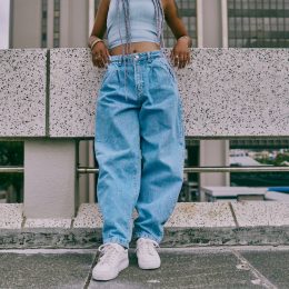 trendy woman in baggy jeans leaning on wall