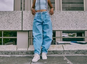 trendy woman in baggy jeans leaning on wall