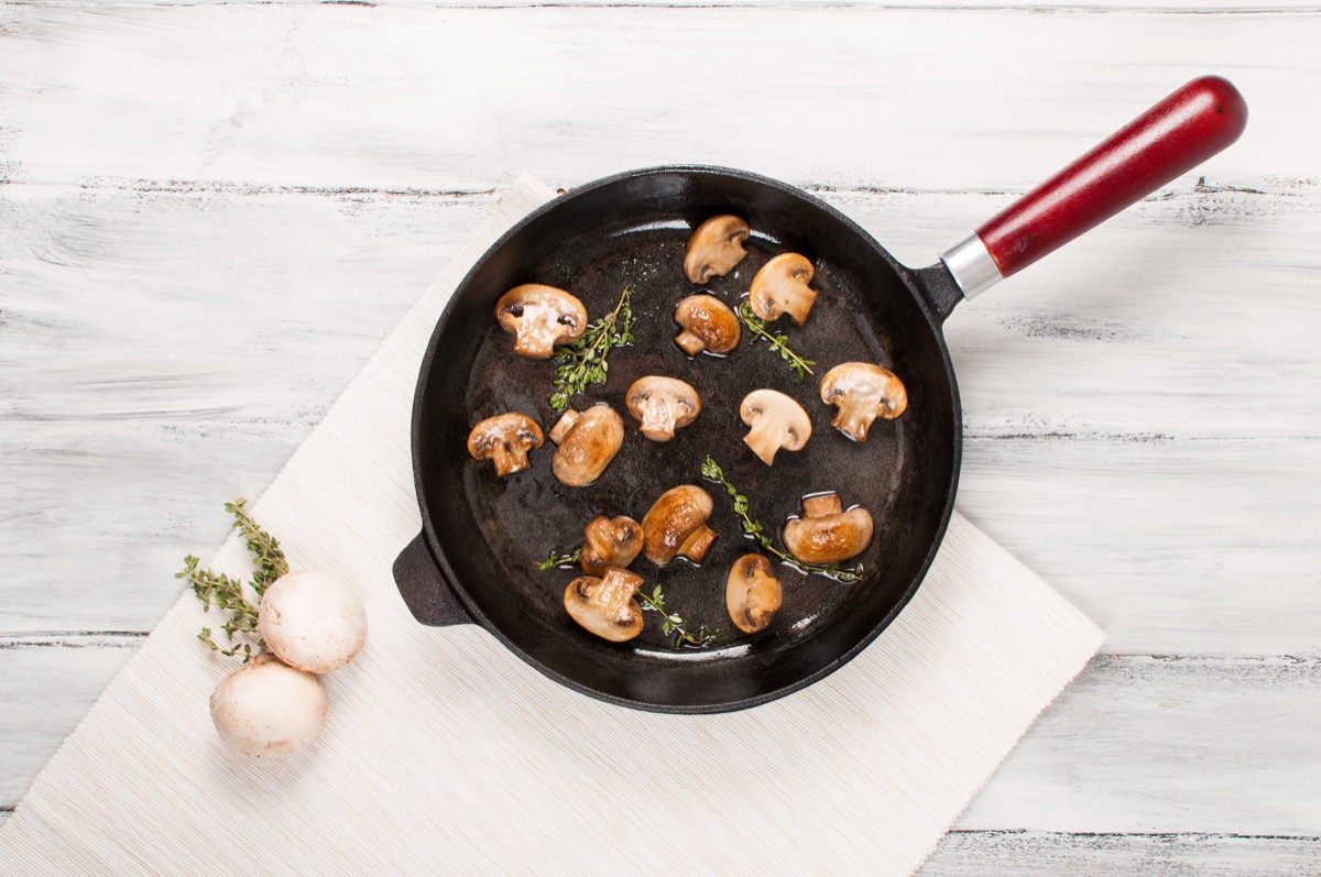Delicious fried mushrooms in a frying pan on a white wooden background