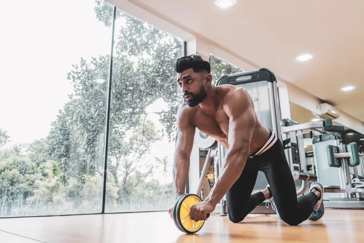 shirtless young man using an ab roller wheel to strengthen his abdominal muscles at the gym