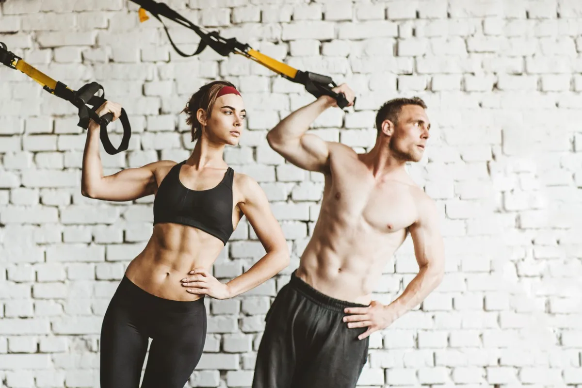 Athletic man and woman doing TRX workout at gym.