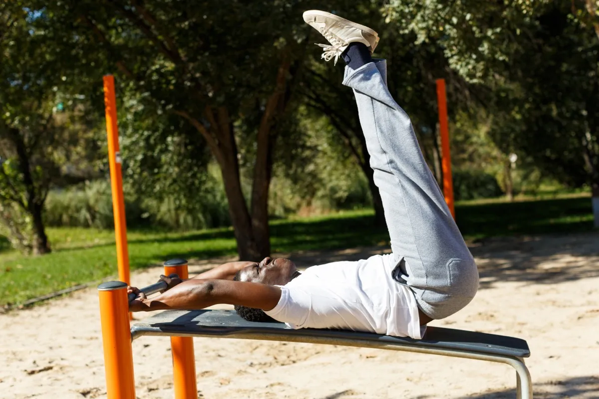 Active young male doing leg raises at sports ground in park outdoor