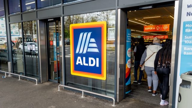 The entrance and exit of a branch of Aldi grocery supermarket with the company name sign and logo in the middle.