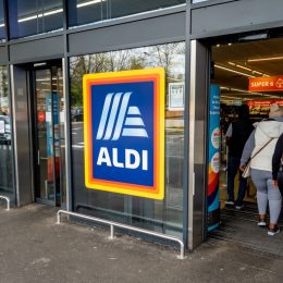 The entrance and exit of a branch of Aldi grocery supermarket with the company name sign and logo in the middle.