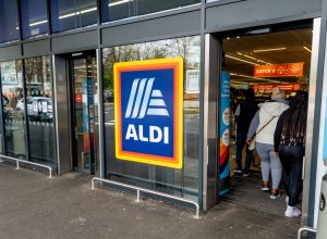 The entrance and exit of a branch of Aldi grocery supermarket with the company name sign and logo in the middle.