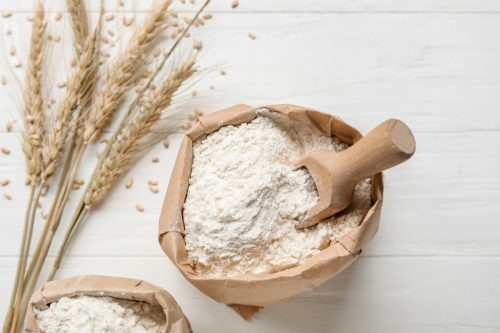 Bags with wheat flour on white wooden background, closeup