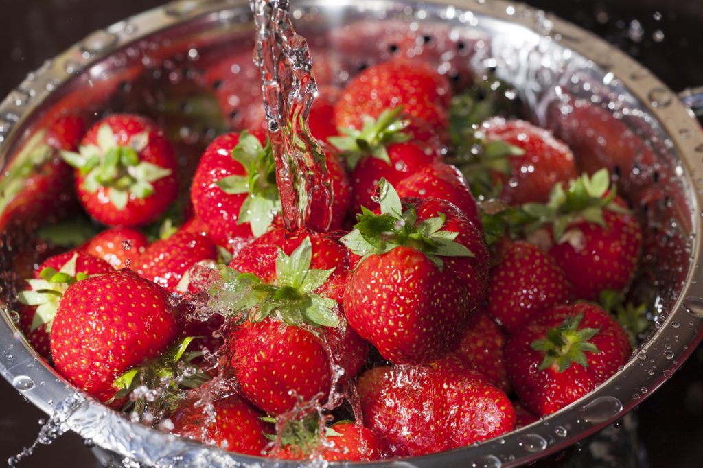 Close up of a strainer filled with strawberries getting washed
