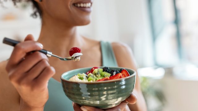Close up of athletic woman eating a healthy fruit bowl in the kitchen at home