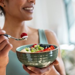 Close up of athletic woman eating a healthy fruit bowl in the kitchen at home