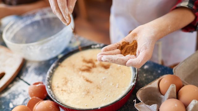 close up of woman's hands as she adds ground cinnamon to a batter