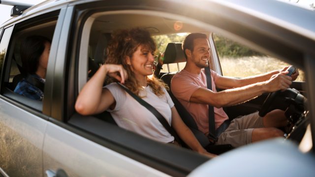 A young couple driving in a car with friends int eh back seat