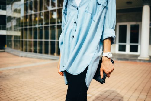 cropped image of a woman wearing black leggings and an oversized denim shirt holding a black clutch while walking outside