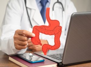 doctor sitting at desk holding out a red cutout of a large intestine