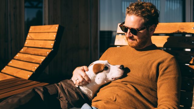 A man lying on a lawn chair with a dog resting on top of him