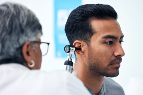 Ear check, man and ENT doctor with patient consultation for hearing and wellness at hospital. Senior, employee and otoscope test of physician with healthcare work and consulting exam with expert
