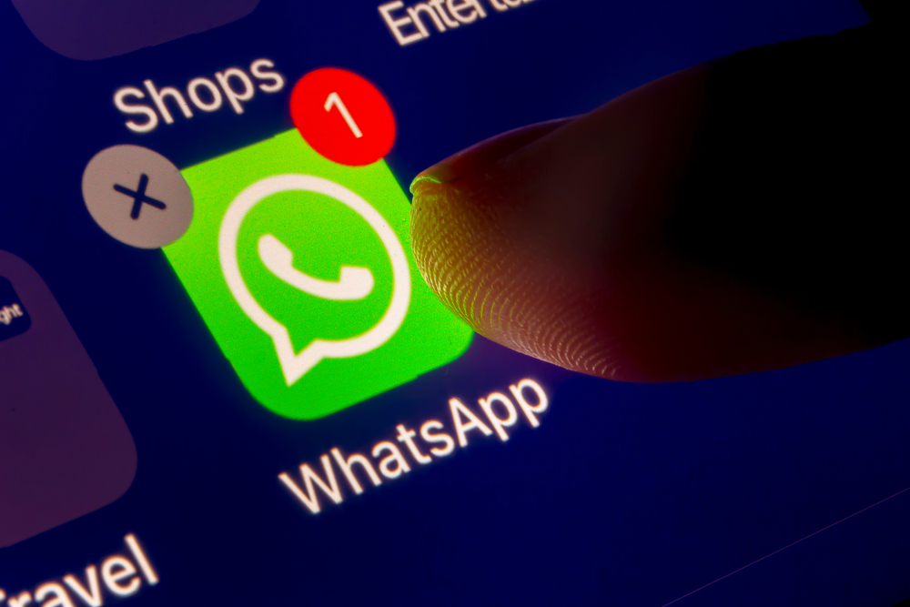 A close up of a finger tapping the WhatsApp icon on a phone