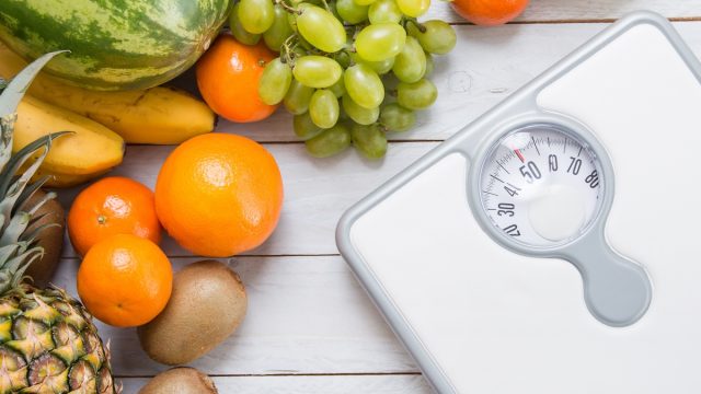 Stack of fruits and white weight scale on wooden board.