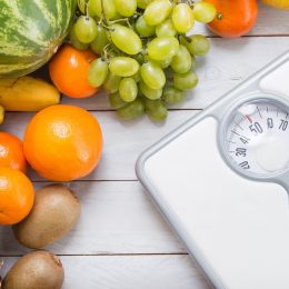 Stack of fruits and white weight scale on wooden board.