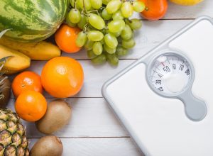 Stack of fruits and white weight scale on wooden board.