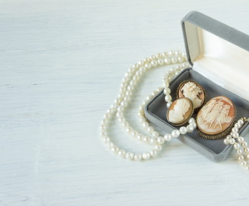Woman's Jewelry. Vintage jewelry background. Beautiful pearl necklace, bracelet and old cameos in a gift box on white wood. Flat lay, top view