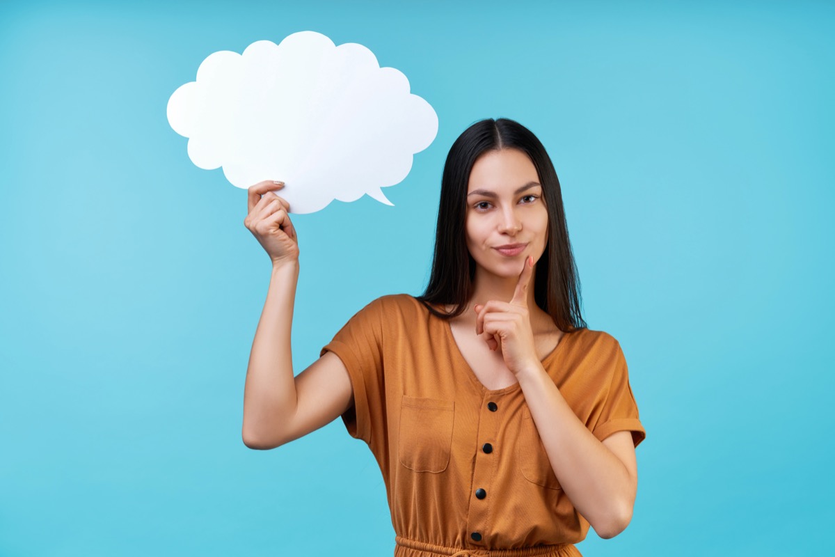 Portrait of woman holding blank paper speech cloud in hand and holding finger on chin