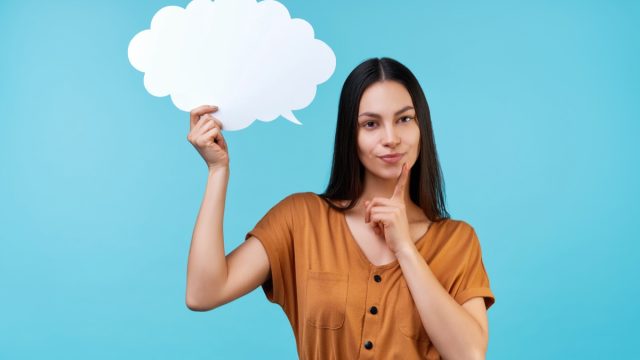 Portrait of woman holding blank paper speech cloud in hand and holding finger on chin