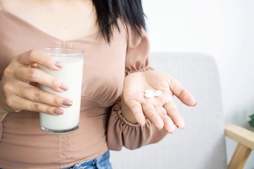 woman holding calcium supplement and glass of milk