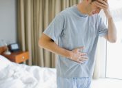 Man standing in bedroom with a stomach ache and headache