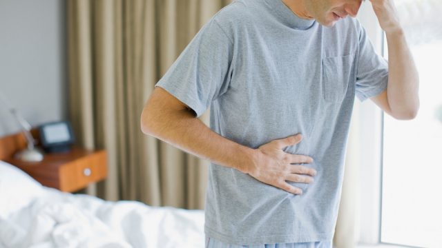 Man standing in bedroom with a stomach ache and headache