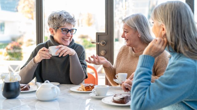 Group of mature women having fun during breakfast while drinking coffee and eating cake
