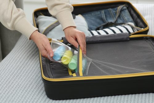 Woman with plastic bag of cosmetic travel kit packing suitcase, closeup. Bath accessories