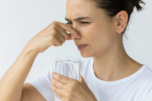 female holding nose and a glass of water in the other hand. Representing bad smell, disgust and water pollution issues.