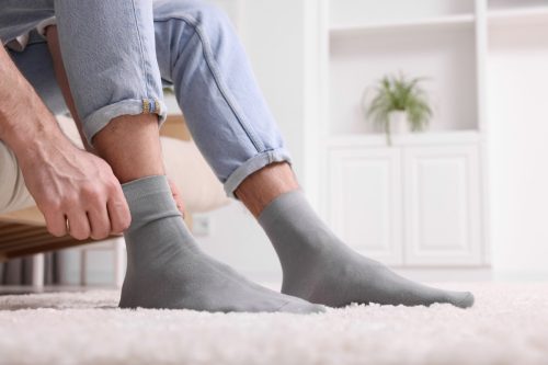 Man putting on grey socks at home, closeup.