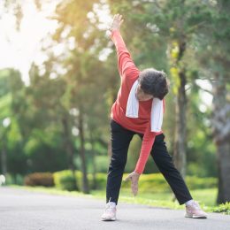 senior woman in black pants and a red top stretching to touch her toes in a park