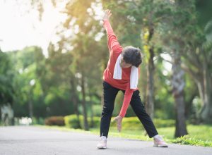 senior woman in black pants and a red top stretching to touch her toes in a park